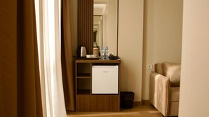 Habitación de hotel con escritorio de madera, refrigerador pequeño, sofá color beige y espejo.