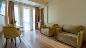 Una camera d'albergo con pavimento in legno, un divano, una poltrona, un tavolino e una finestra con tende.