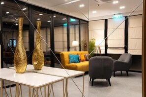 Um interior moderno com uma mesa branca, dois vasos dourados, um sofá amarelo e cadeiras cinzentas.