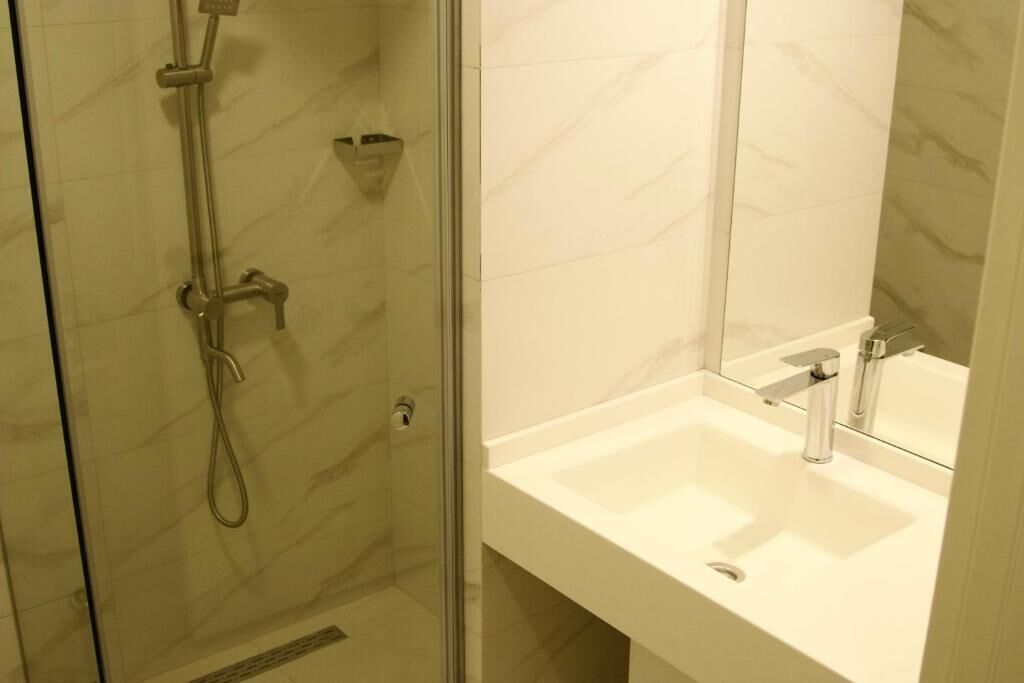 A bathroom with a glass-enclosed shower, a white sink, and a mirror.