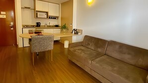 Una sala de estar con un sofá marrón, una silla estampada y una cocina al fondo.