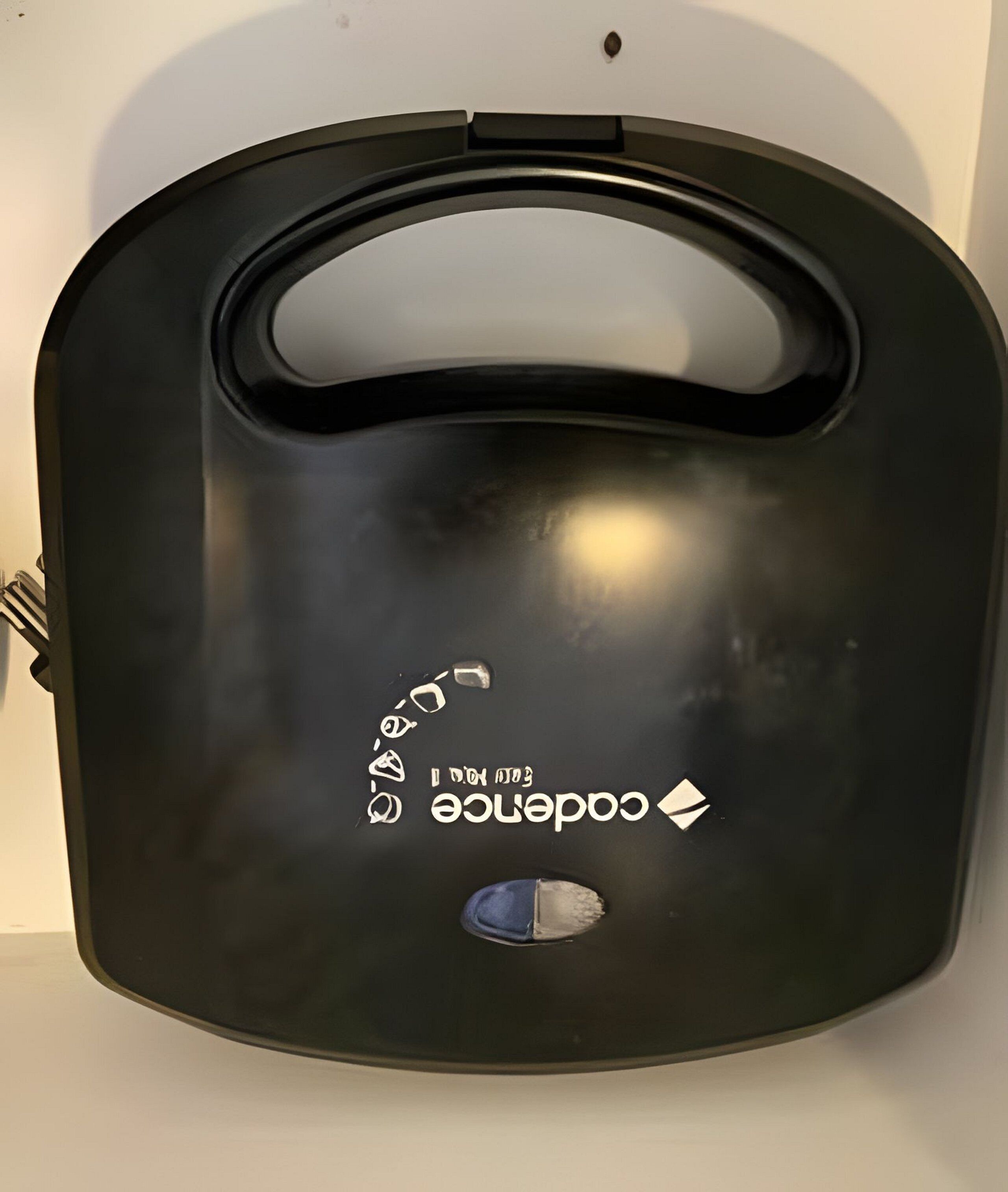 Um recipiente retangular preto, metálico, com uma alça e uma pequena abertura circular, provavelmente para armazenar ou preparar alimentos.