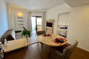 Quarto de hotel moderno com área de refeições, sofá, televisão e cama.