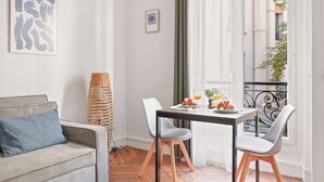 Ein modernes Wohnzimmer mit einer Couch, einem Esstisch mit Stühlen, einer Korbmöbel-Stehlampe und Blick auf die Stadt durch ein Fenster.