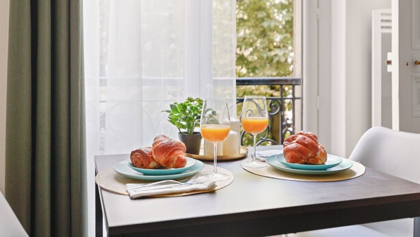 Ein Esstisch mit Croissants, einem Glas Orangensaft und einer Topfpflanze.