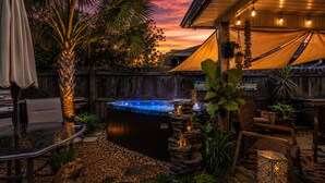 Ein Whirlpool, umgeben von Gartenmöbeln, einem Holzzaun und einem Sonnenuntergangshimmel.