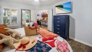 Ein Schlafzimmer mit einem Bett, einem Kleiderschrank, einem Fernseher und Blick auf einen Strand durch das Fenster.