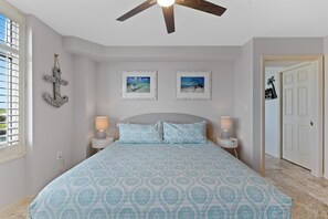 A bedroom with a bed, two wall-mounted lamps, a ceiling fan, and two framed pictures.