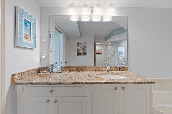 A bathroom with a granite countertop, a sink, a mirror, and a shower.