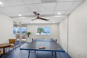 Ein Tischtennistisch in einem Raum mit Deckenventilator, großen Fenstern und Blick ins Freie.