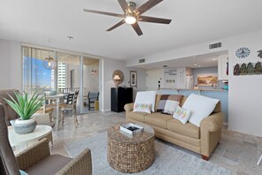 Ein geräumiges Wohnzimmer mit Deckenventilator, Esstisch mit Stühlen, einer Couch mit dekorativen Kissen und einem Couchtisch.