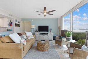 A spacious living room with a ceiling fan, a television, and a large window offering a view of the city.