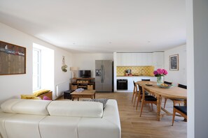 A modern living room with a sofa, a dining table with chairs, a kitchen area with appliances, and a TV. - Bright house, 2 minutes from the beach and town center (Piriac-sur-Mer)