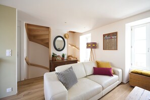 A living room with a sofa, a wooden staircase, a mirror, and a painting on the wall. - Bright house, 2 minutes from the beach and town center (Piriac-sur-Mer)