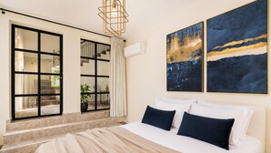 Un dormitorio con una cama grande, una ventana con vistas al exterior y dos cuadros abstractos en la pared.