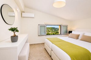 A bedroom with a bed, a bedside table, a potted plant, a window with a view, and an air conditioning unit. - Kaletzia Villa IV - Four Bedroom Villa, Sleeps 8 (Zakinthos)
