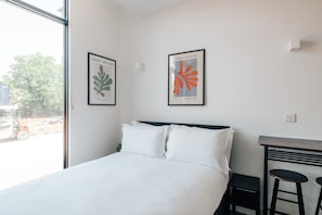 Une chambre d’hôtel avec un lit, deux œuvres d’art encadrées, une fenêtre et une petite table avec deux tabourets.