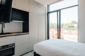 Ein modernes Hotelzimmer mit einem Bett, einem eingebauten Backofen, einem Fernseher und einem großen Fenster mit Blick auf eine Baustelle im Freien.