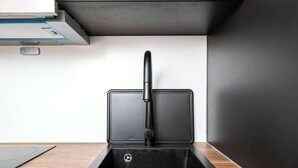 Een keuken met een zwart spoelbak, een kraan en een inbouwafzuigkap.