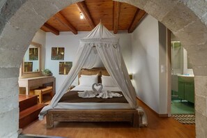 Ein Schlafzimmer mit einem Himmelbett, einer Holzbank, einem Schminktisch mit Spiegel und einem grünen Schrank.