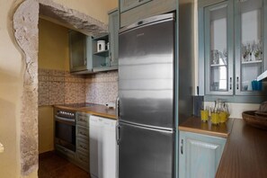 Eine Küche mit einem Edelstahl-Kühlschrank, einem Geschirrspüler, einem Backofen und einer Spüle. Es gibt eine geflieste Rückwand und ein steinernes Rundbogenportal.