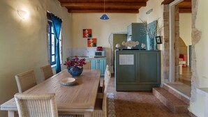 Un comedor con mesa de madera y sillas de mimbre, una cocina con un mueble verde y una pared de piedra.