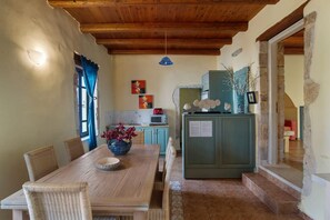 Ein Essbereich mit Holztisch und Korbstühlen, eine Küche mit einem grünen Schrank und eine Steinwand.