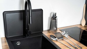 A kitchen with a black sink, a faucet, a grater, a spatula, a spoon, and a pair of tongs. - Cosy Victorian studio near The O2 & Greenwich (London)