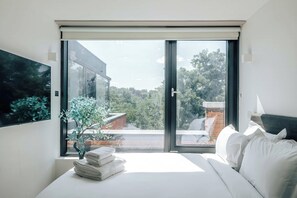 A modern bedroom with a large sliding glass door leading to a balcony, a bed with white bedding, and a small potted plant. - The Antigallican by Nestor | Cosy studio (London)