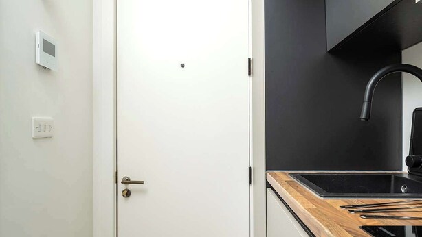 A modern kitchen with a black faucet, a wooden countertop, and a white door. - Cosy Victorian studio near The O2 & Greenwich (London)