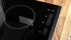 A black induction cooktop with a circular control area and various buttons. - Cosy Victorian studio near The O2 & Greenwich (London)