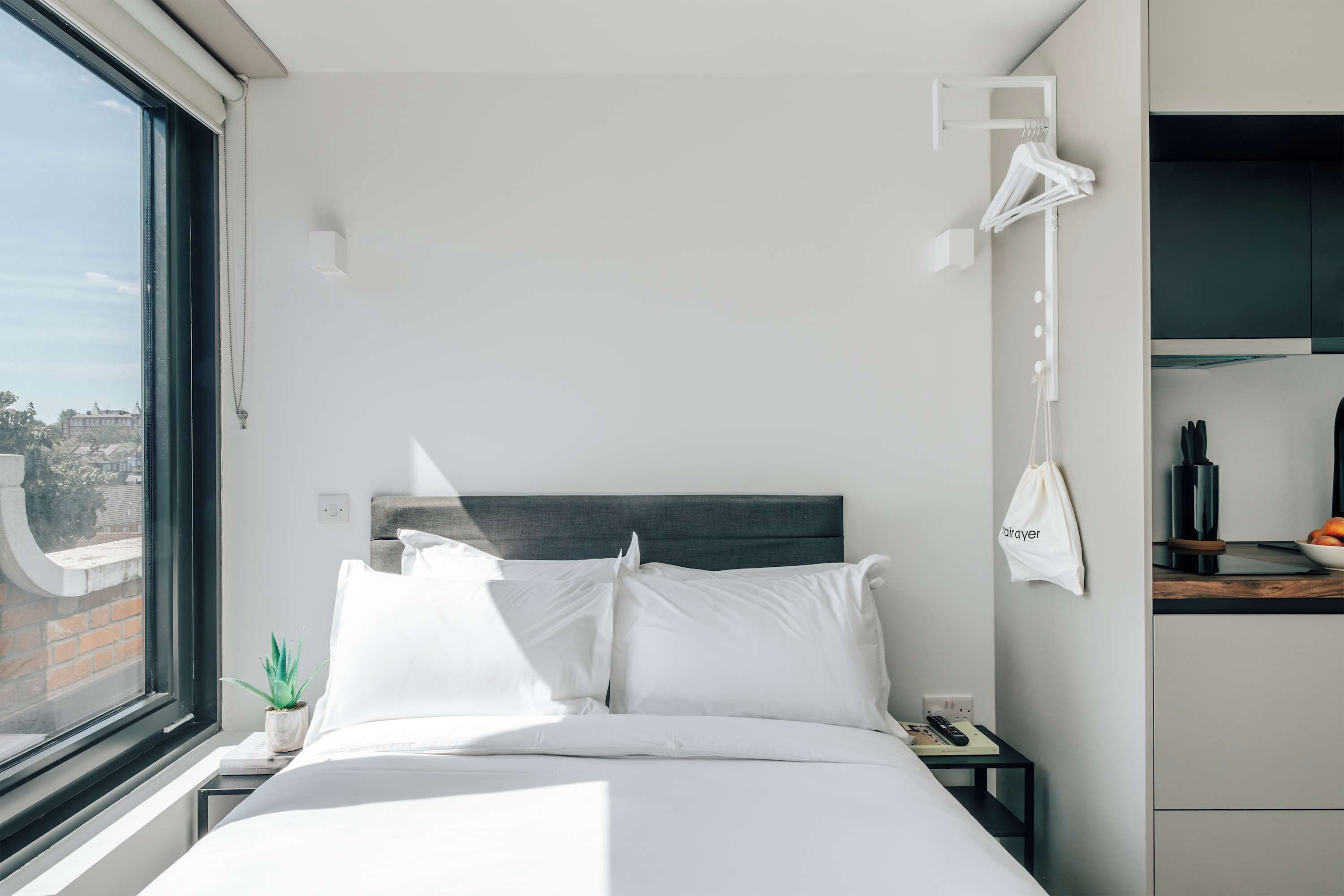 Ein Hotelzimmer mit Bett, Nachttisch mit Lampe, Handtuchhalter und Blick ins Freie.