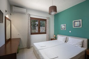 Ein Schlafzimmer mit einem Bett, einem Fenster, einer Klimaanlage, einer Lampe und zwei gerahmten Bildern an der Wand.