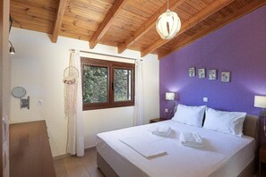 Ein Schlafzimmer mit Holzboden, einem Bett mit weißen Bettbezügen, einem Fenster mit Vorhängen und Wandlampen.