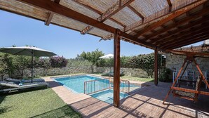 A swimming pool with a wooden deck, lounge chairs, and a pergola structure. - Villa Portokalia - Two Bedroom Villa, Sleeps 4 (Platanias)
