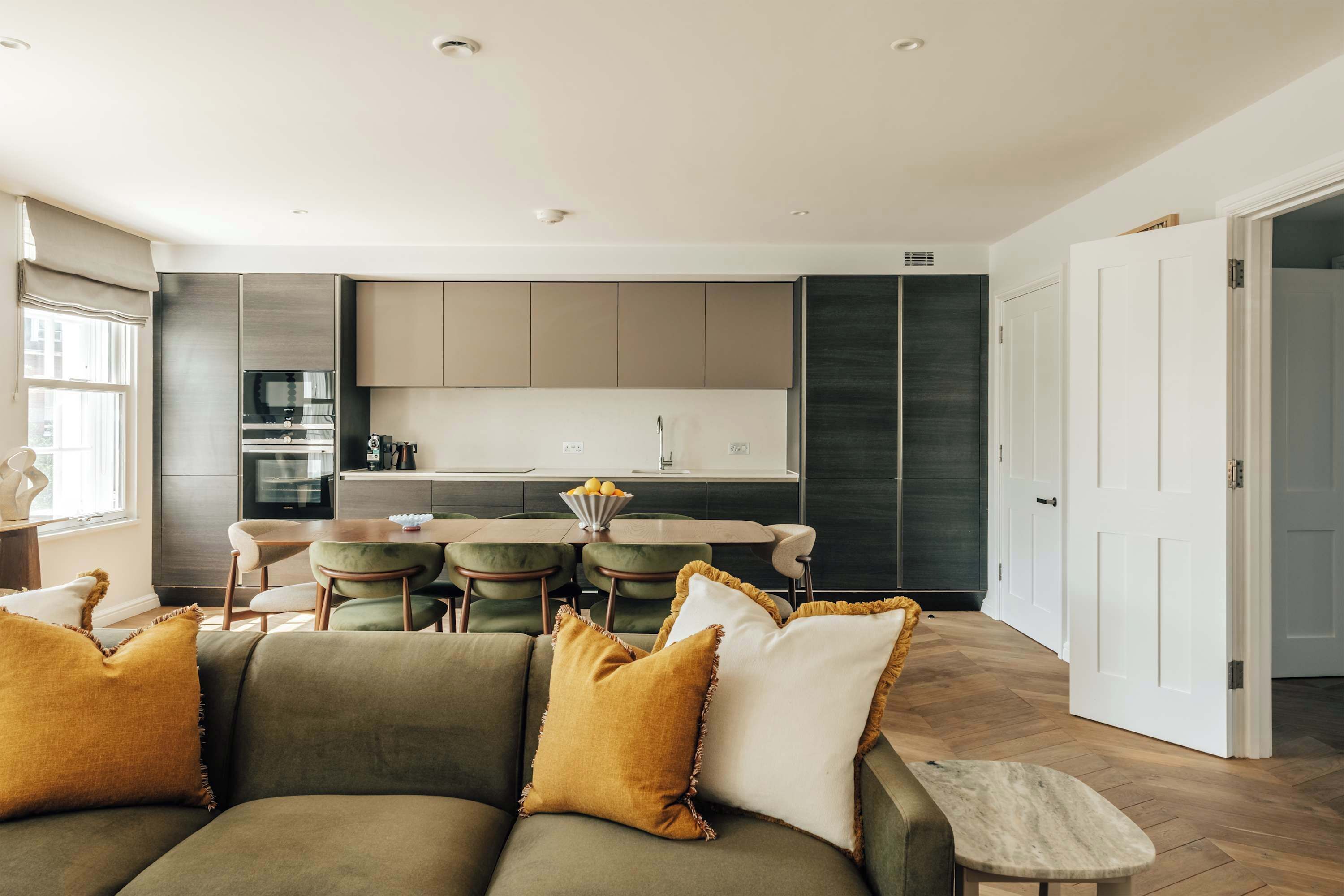 Una sala de estar moderna con un sofá y sillones, un comedor con mesa y sillas, y una cocina con armarios y electrodomésticos.