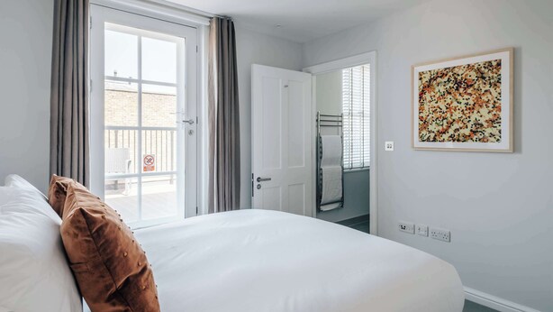 A hotel room with a bed, a door leading to a balcony, and a framed artwork on the wall. - Premium 3-Bed Belgravia | Sloane Square (London)