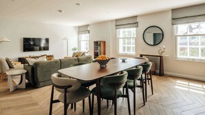 A modern living room with a sofa, a dining table with chairs, a TV mounted on the wall, and a large window with curtains. - Premium 3-Bed Belgravia | Sloane Square (London)