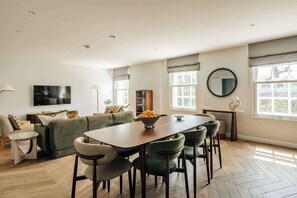 A modern living room with a dining area, large windows, and a flat-screen TV. - Premium 3-Bed Belgravia | Sloane Square (London)