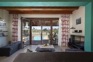Un saló amb televisió, sofà, taula de centre i vista a una piscina exterior.