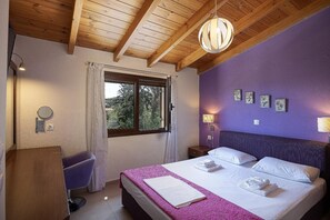 A hotel room with a bed, a desk, a chair, a window, and a ceiling with wooden beams. - Villa Lemonia - Two Bedroom Villa, Sleeps 4 (Platanias)