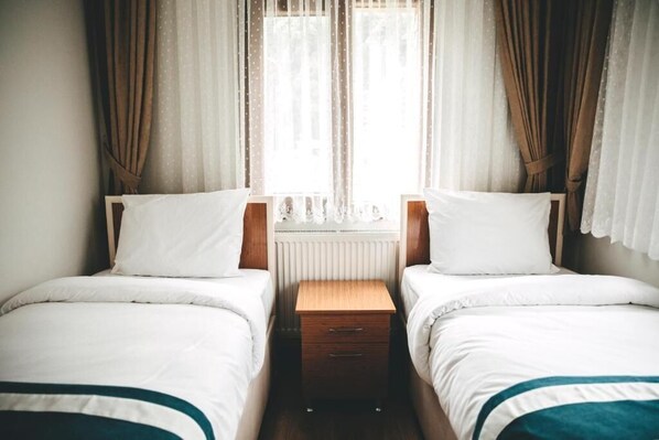 Une chambre double avec deux lits, une table de chevet en bois et une fenêtre avec des rideaux.