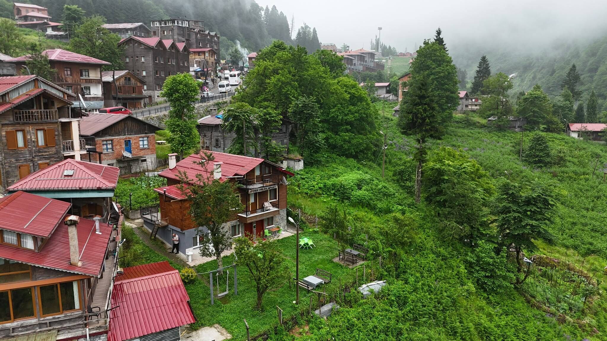 Un villaggio montano con case in legno tradizionali, una strada asfaltata e vegetazione lussureggiante.