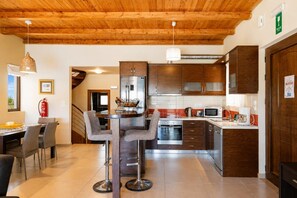 A modern kitchen with wooden cabinets, stainless steel appliances, and a dining area with a table and chairs. - Villa Mandarin - Two Bedroom Villa, Sleeps 4 (Platanias)