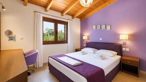 A bedroom with a bed, bedside tables, a nightstand, a window with curtains, a hanging light fixture, and wall art. - Villa Mandarin - Two Bedroom Villa, Sleeps 4 (Platanias)