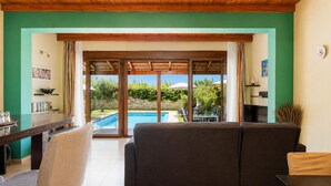 A living room with a sofa, a dining table, and a view of a swimming pool. - Villa Mandarin - Two Bedroom Villa, Sleeps 4 (Platanias)