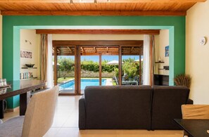 A living room with a sofa, a dining table, and a view of a swimming pool. - Villa Mandarin - Two Bedroom Villa, Sleeps 4 (Platanias)