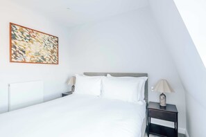 Een slaapkamer met een bed, twee nachtkastjes, een lamp en een wanddecoratie met abstracte vormen.