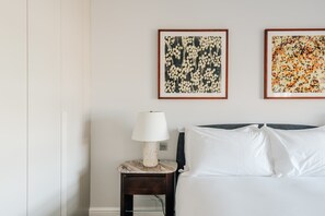 A bedroom with a bed, a nightstand with a lamp, and two framed floral artworks on the wall. - Deluxe 2-Bed Belgravia | Sloane Square (London)