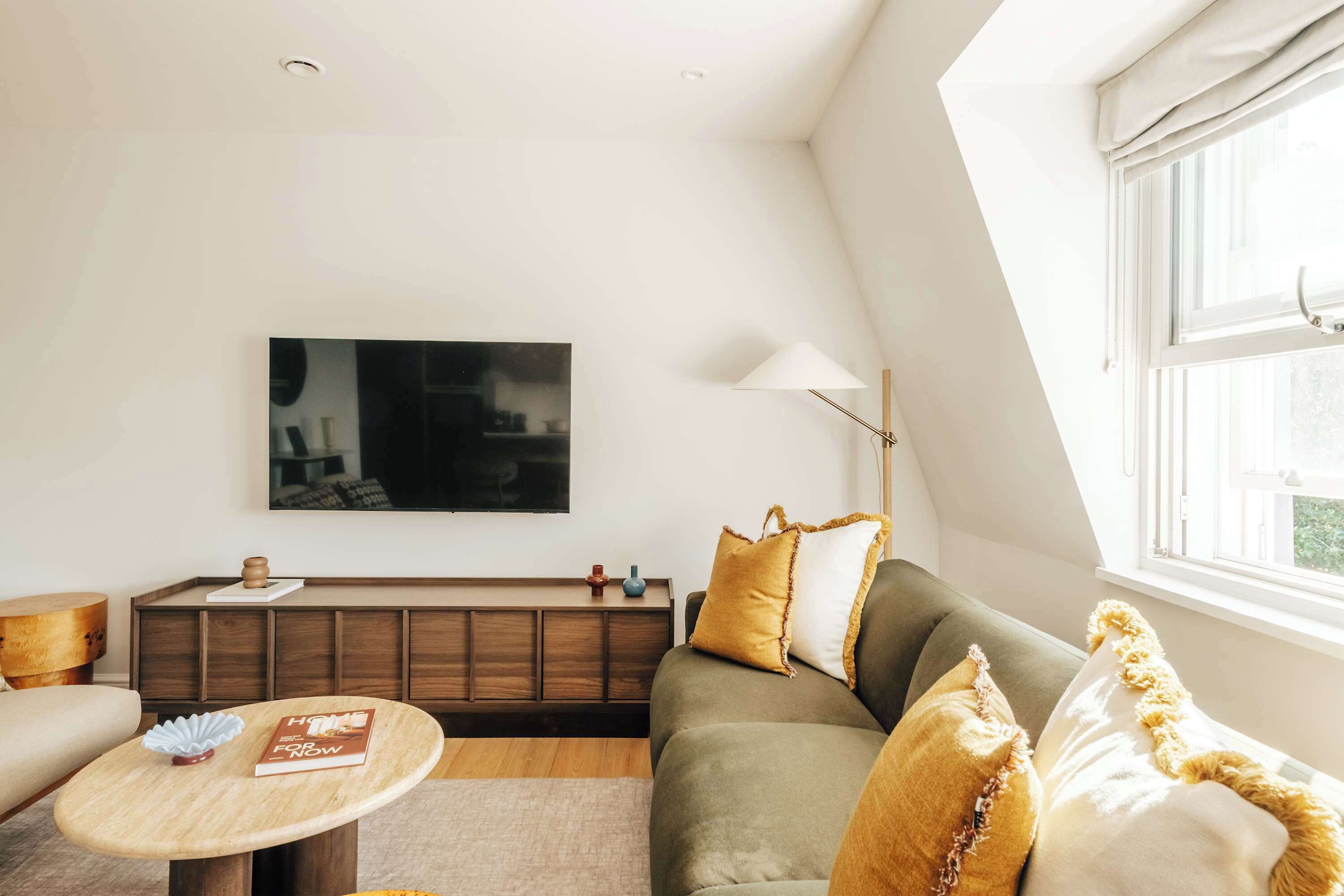 En moderne stue med sofa, sofabord, fladskærms-tv og et vindue med gardiner.